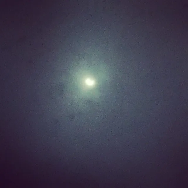 Un disc luminos și strălucitor se află în centrul unui cer întunecat și granulat.