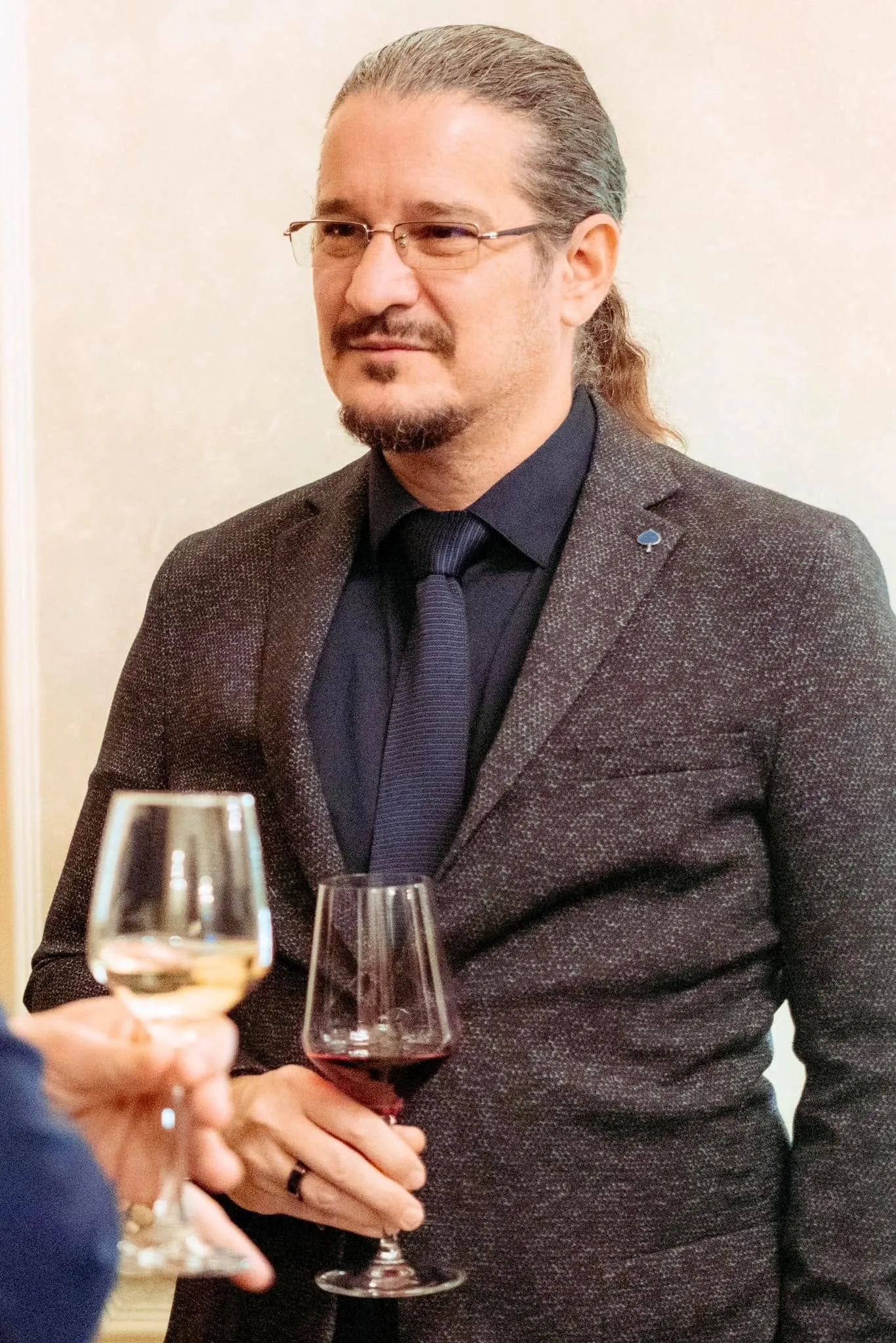 Sebastian Cochinescu, îmbrăcat elegant, stă la o recepție ținând în mână un pahar cu vin roșu.