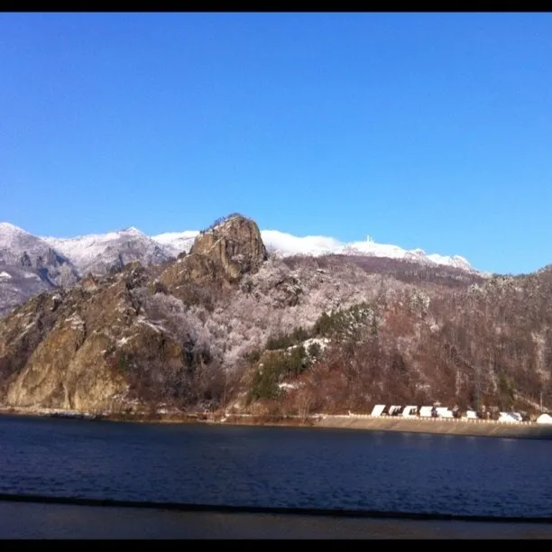 Dam in the Olt Valley with a snow-covered rocky mountain under a clear blue sky