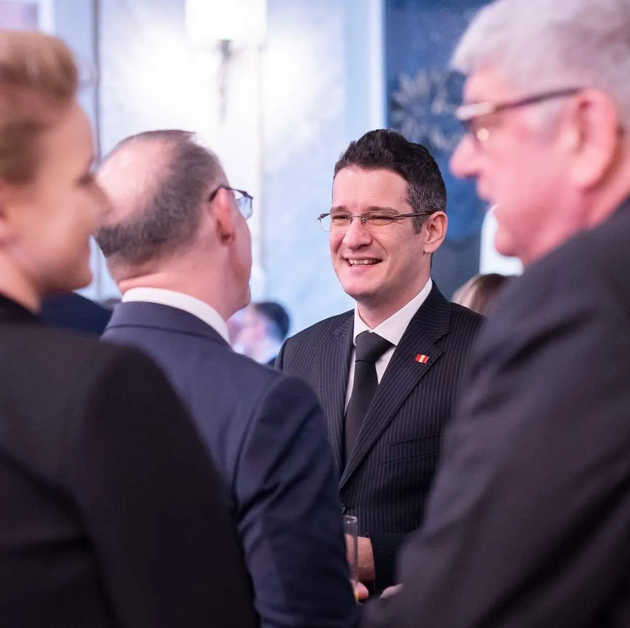Sebastian Cochinescu zâmbește în timp ce vorbește cu invitații la o recepție oficială.