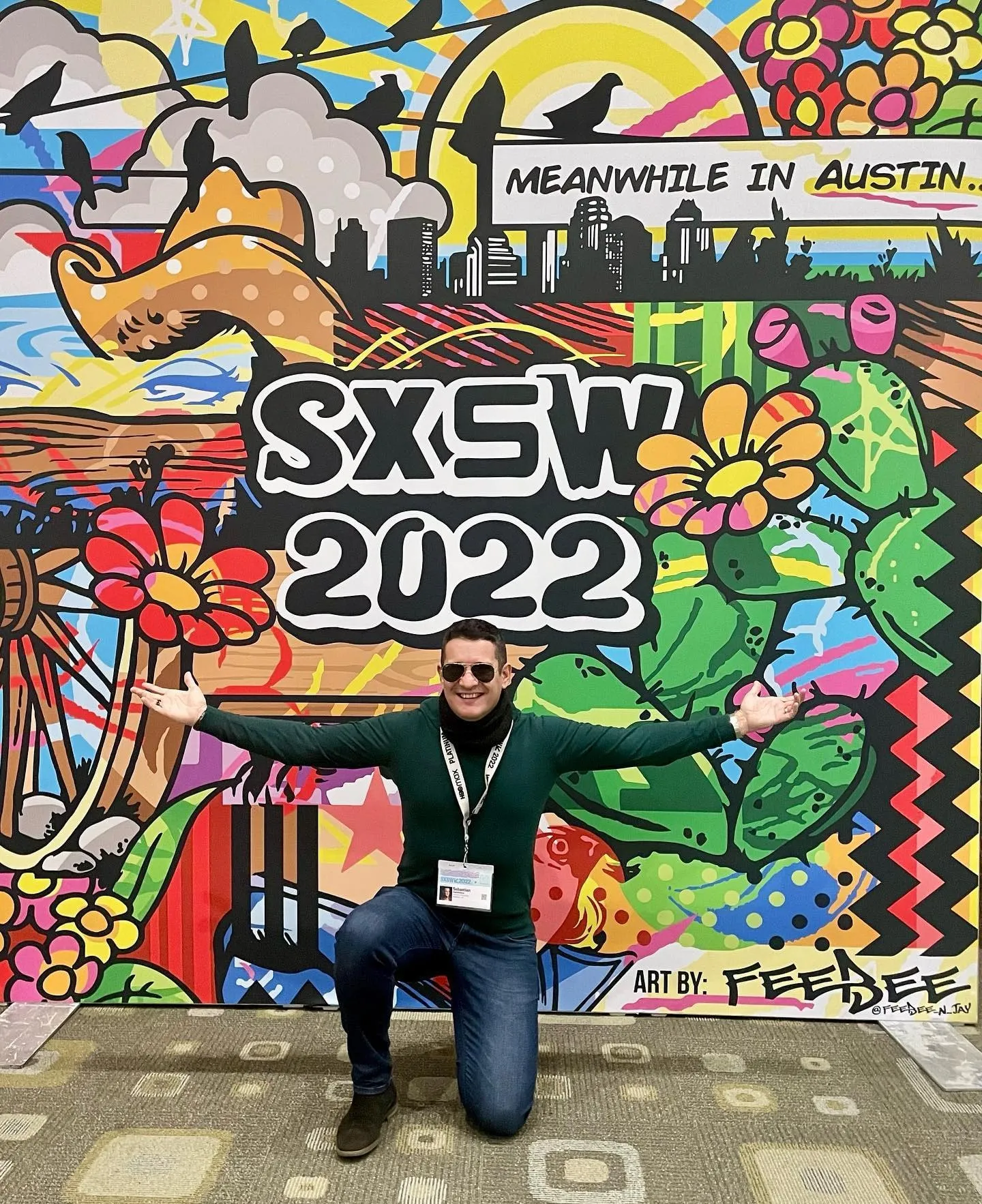 Sebastian Cochinescu pozează cu brațele deschise în fața unei picturi murale colorate SXSW 2022.