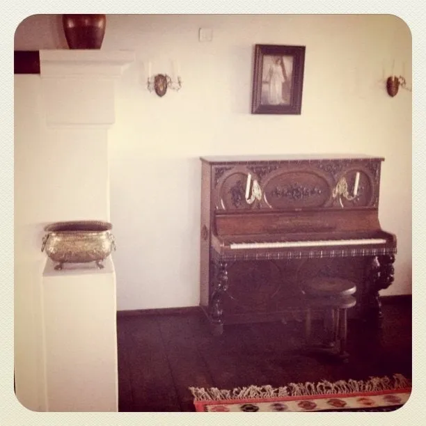 An ornate wooden upright piano in a room at Bran Castle, with a chair and a painting on the wall.