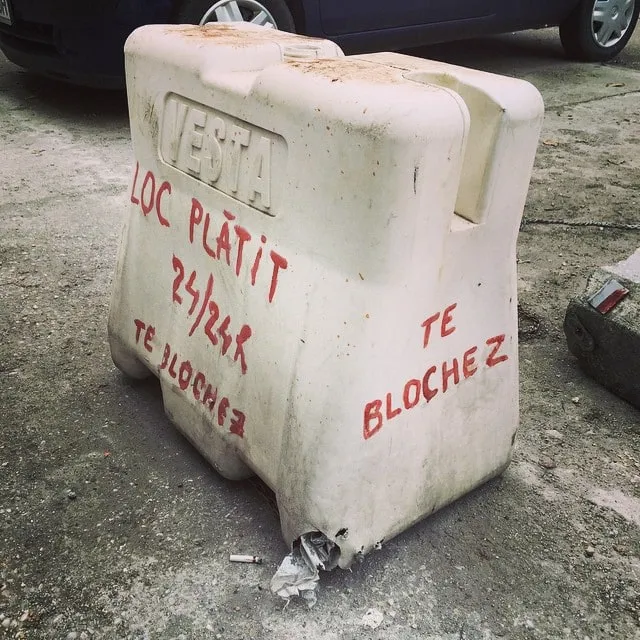 A white plastic Vesta barrier on asphalt marked in red with Loc plătit 24/24 and Te blochez.