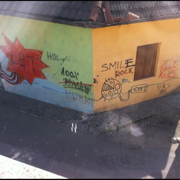 Colț de casă cu pereți galben și verde, graffiti și acoperiș de țiglă, în Bistrița.