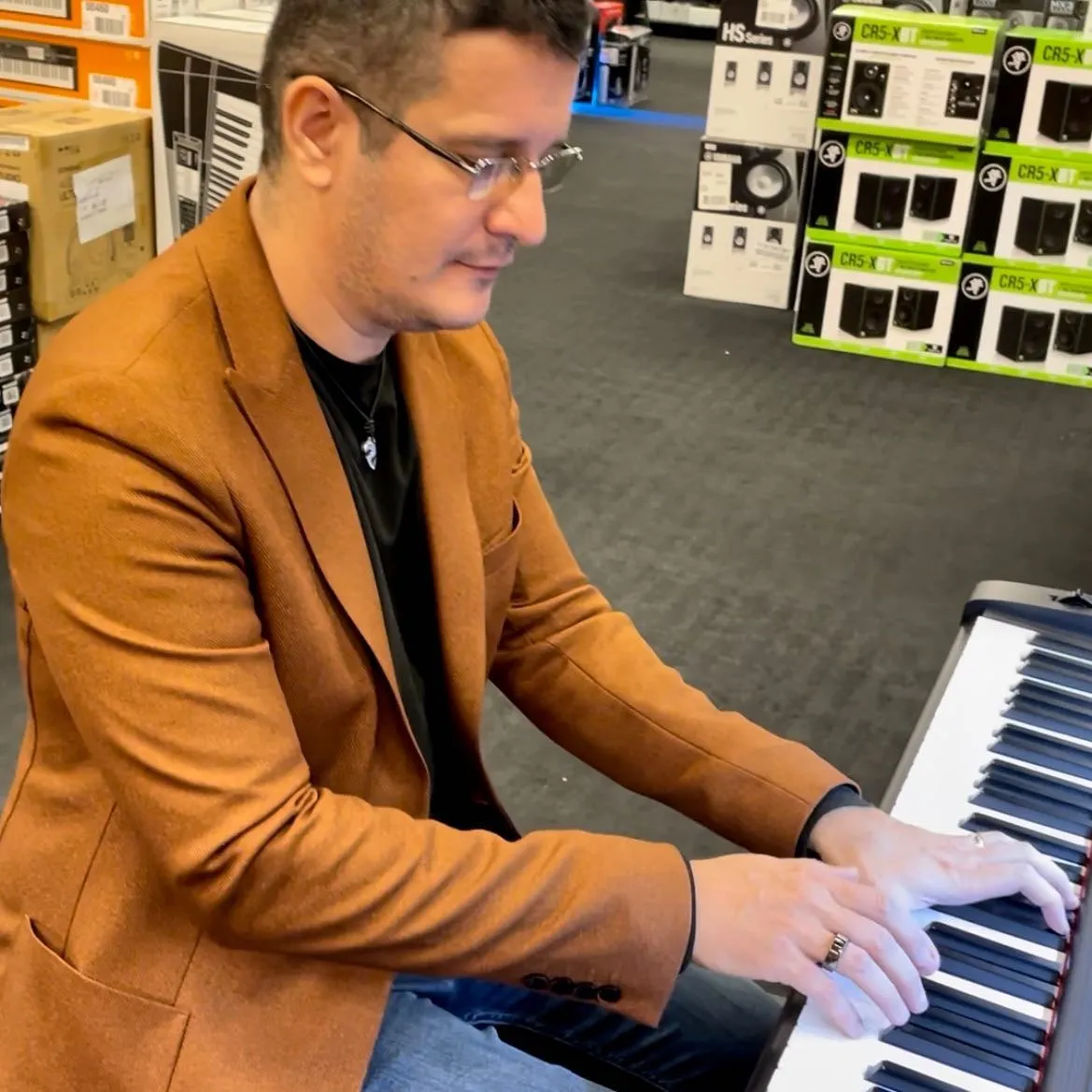 Sebastian Cochinescu cântă la o claviatură electronică, așezat într-un magazin de instrumente muzicale.