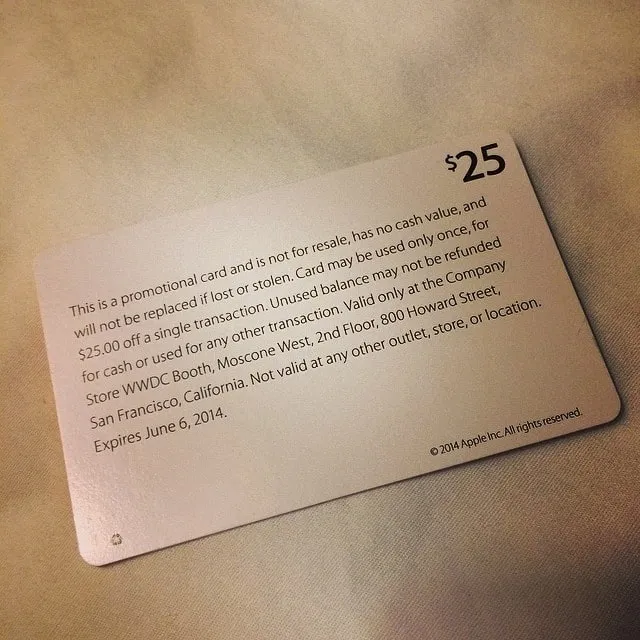 A beige Apple promotional gift card for $25 off at the WWDC booth in San Francisco, resting on fabric.