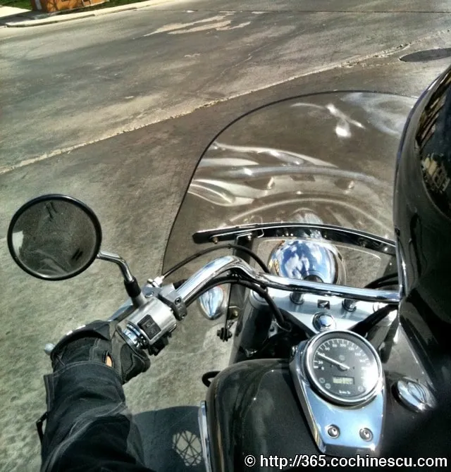 The motorcyclist looks over the handlebar and windshield of a motorcycle stopped in the street.