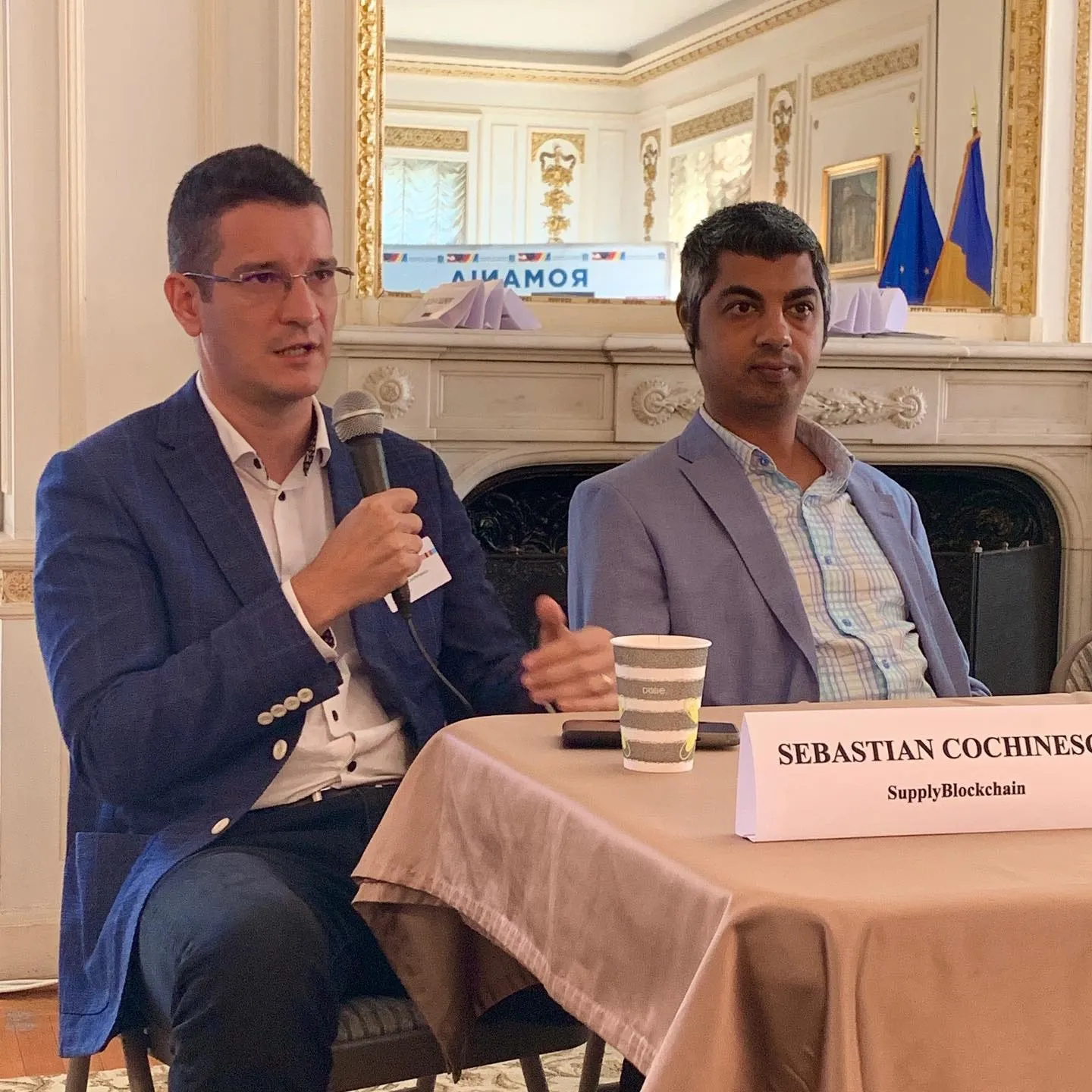 Sebastian Cochinescu vorbește la microfon, alături de un alt participant la discuție, la Ambasada României din Washington, DC.