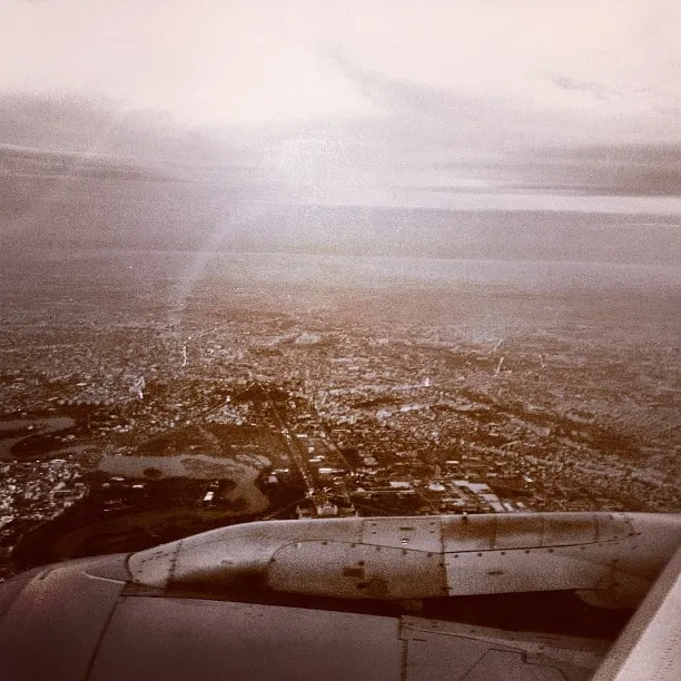 Aerial view of the city from a plane, with the plane’s wing in the foreground under a cloudy sky.