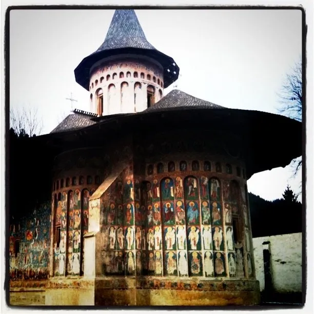 Exteriorul bisericii de la Mănăstirea Voroneț, acoperit cu fresce murale colorate sub un acoperiș întunecat