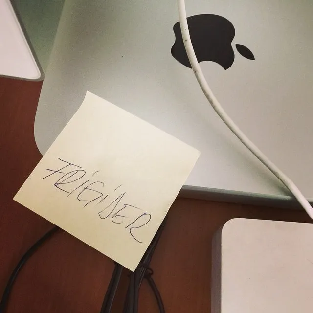 Sticky note galben cu textul Frigider lipit pe spatele unui iMac argintiu cu logo Apple