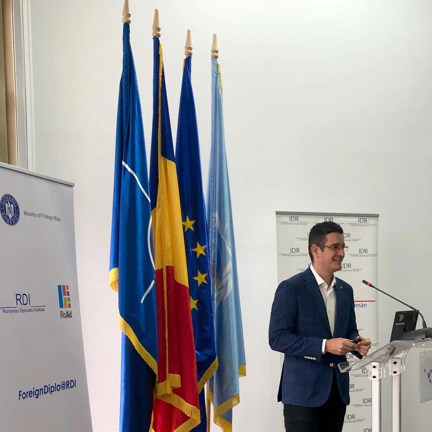 Sebastian Cochinescu speaks at a lectern beside Romanian, European Union, NATO, and United Nations flags.