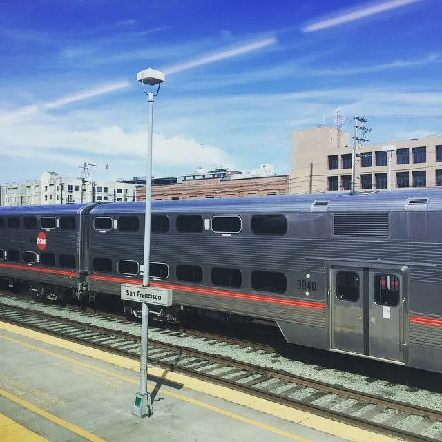 Tren Caltrain cu etaj pe peronul gării din San Francisco, sub un cer albastru cu nori.