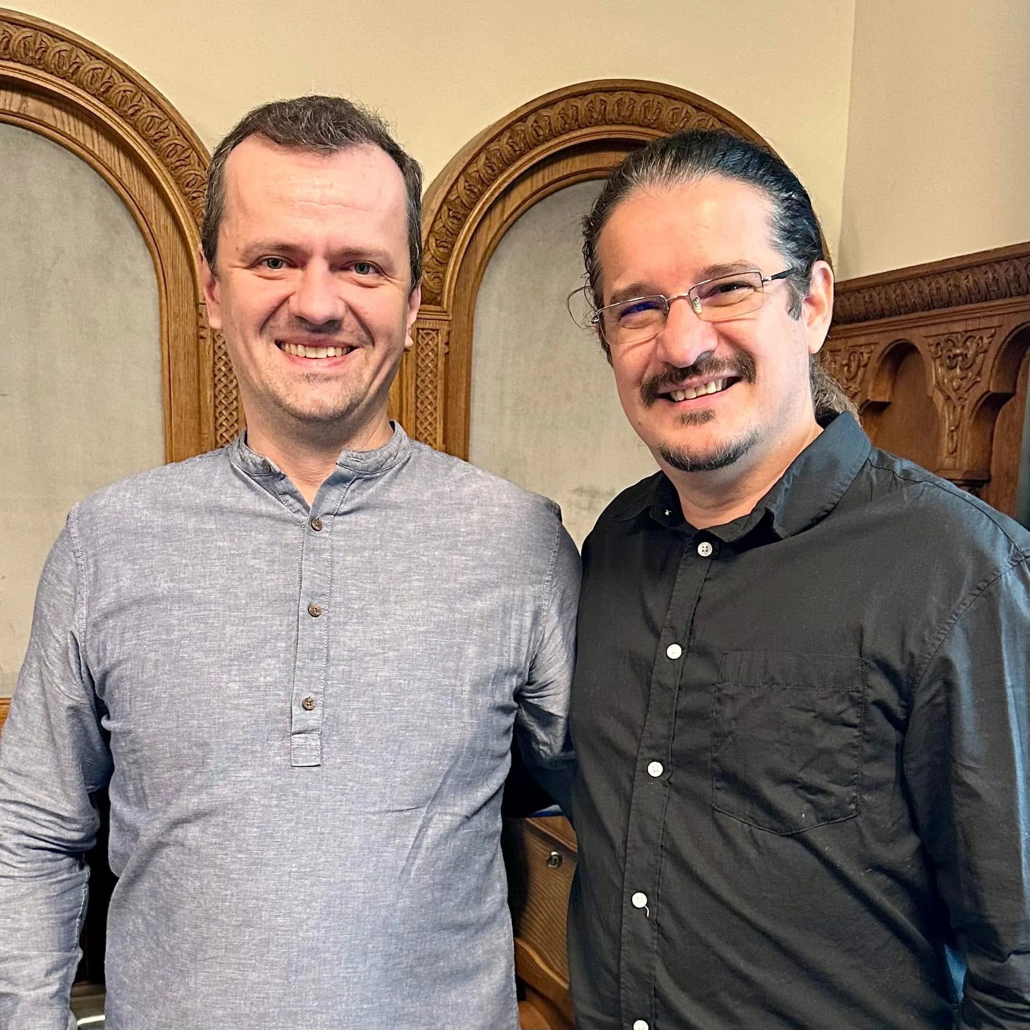 Marius Istrate și Sebastian Cochinescu stau împreună, zâmbind, într-o încăpere elegantă, cu pereți lambrisați din lemn.