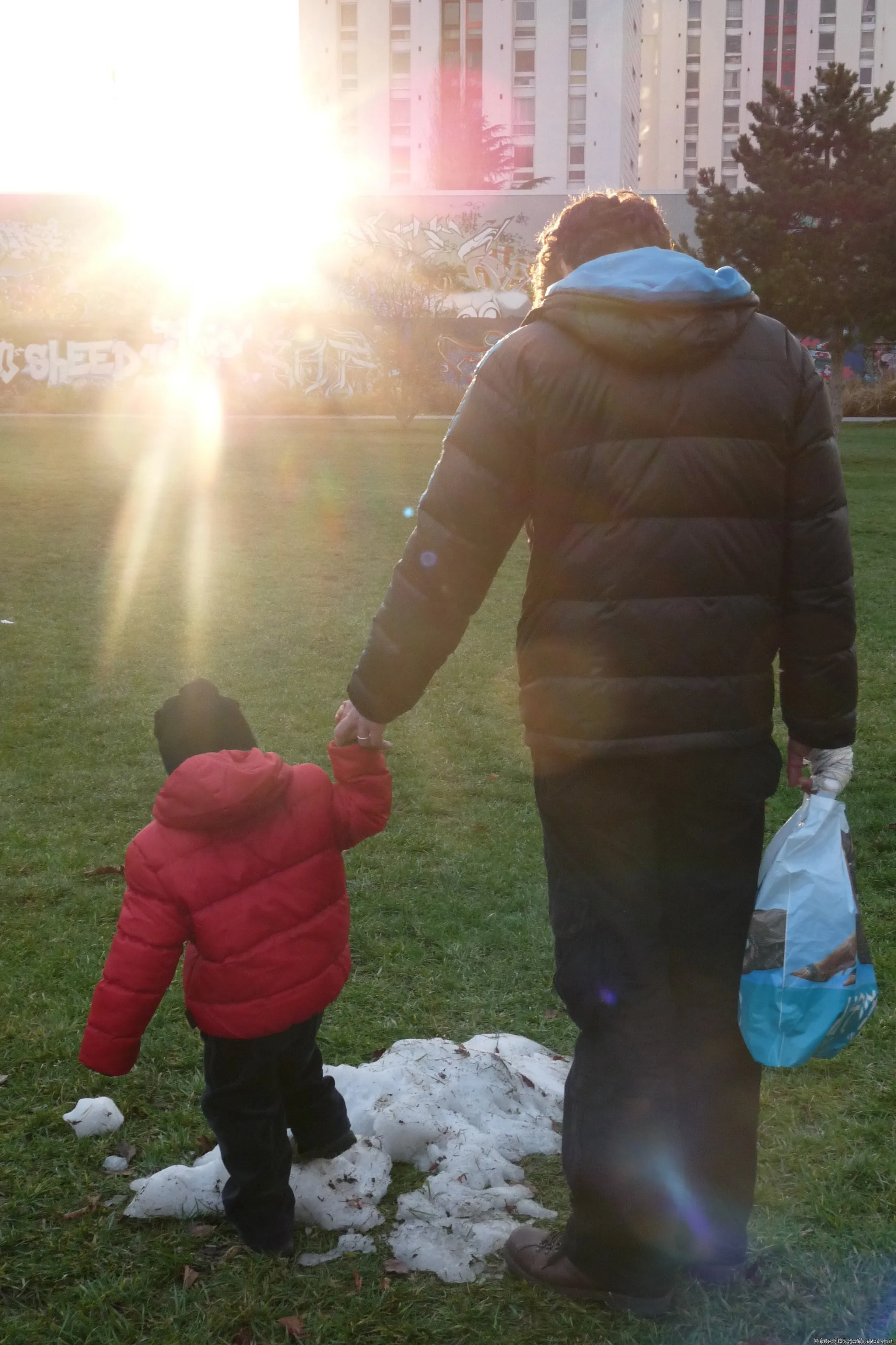 Un adult și un copil merg de mână printr-un petic de zăpadă, în lumina apusului.