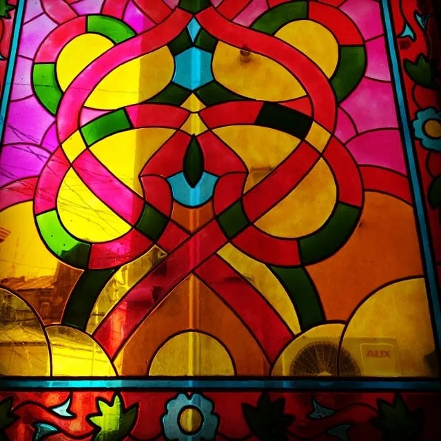 Colorful stained glass with red, yellow, and green patterns, with an AUX air conditioner visible through it.