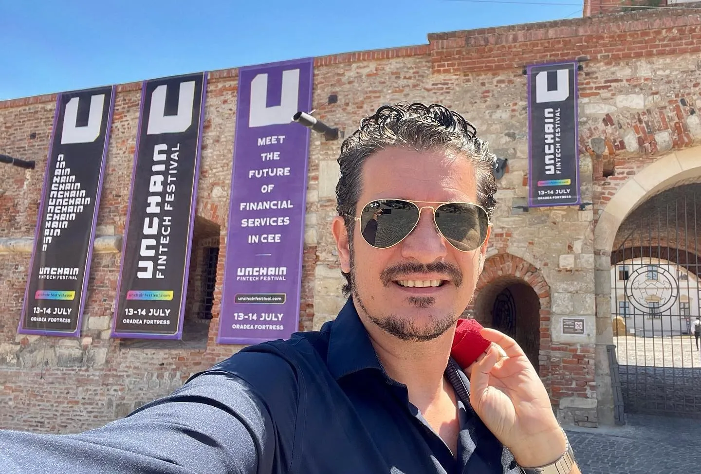 Sebastian Cochinescu takes a selfie outside Oradea Fortress beneath banners for the Unchain Fintech Festival.