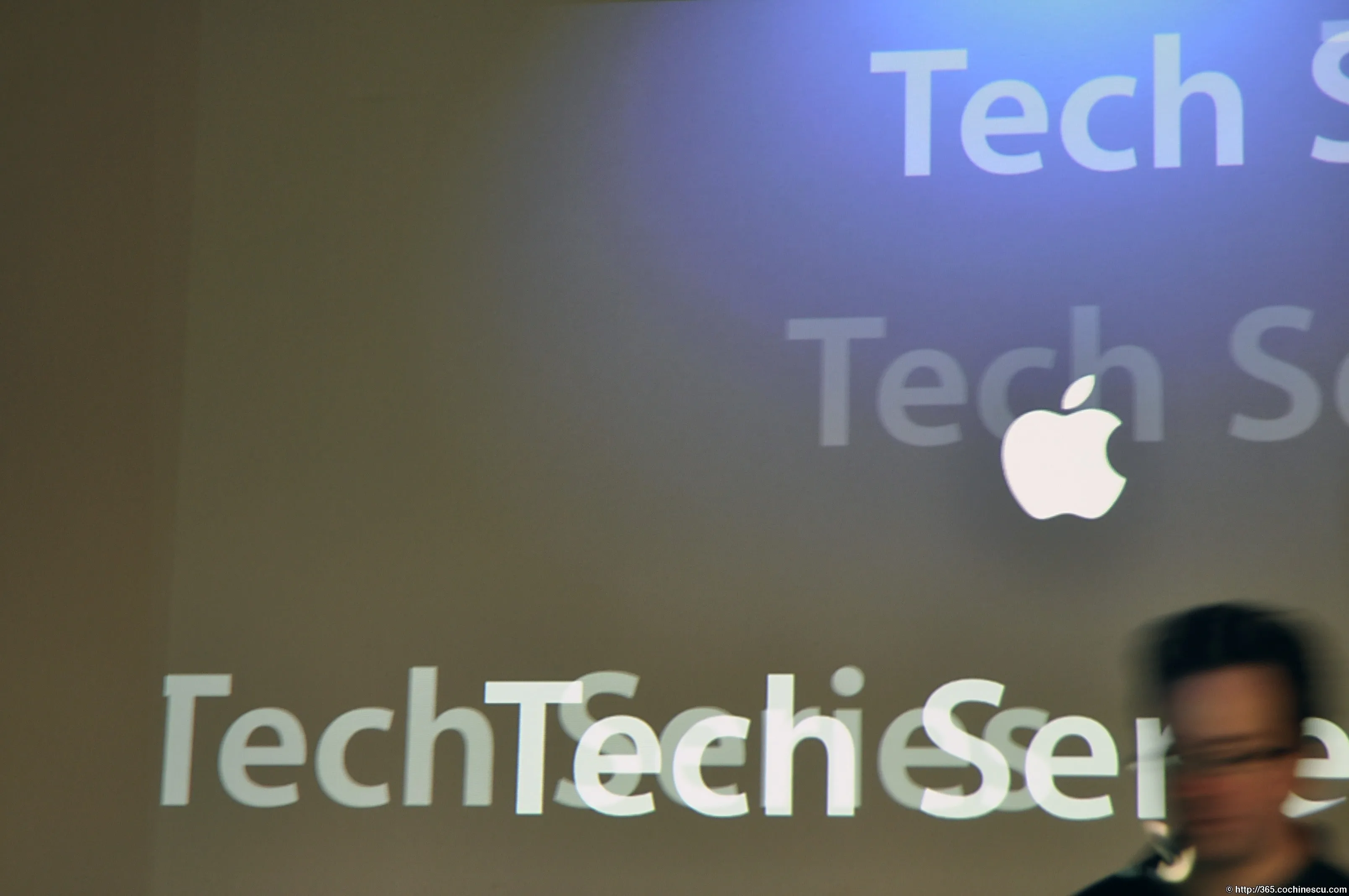 The Apple logo is projected over the text Tech Series, while a person walks through the frame.