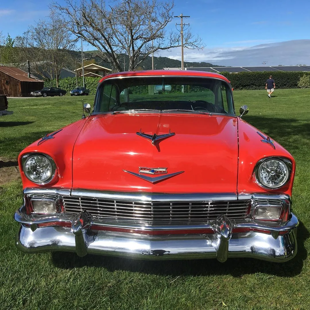 Front view of a bright red classic 1950s Chevrolet with chrome bumper and grille parked on green grass